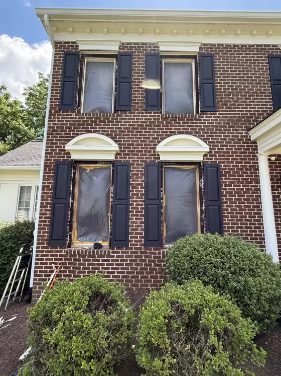 Brick house facade with windows covered in protective film during replacement