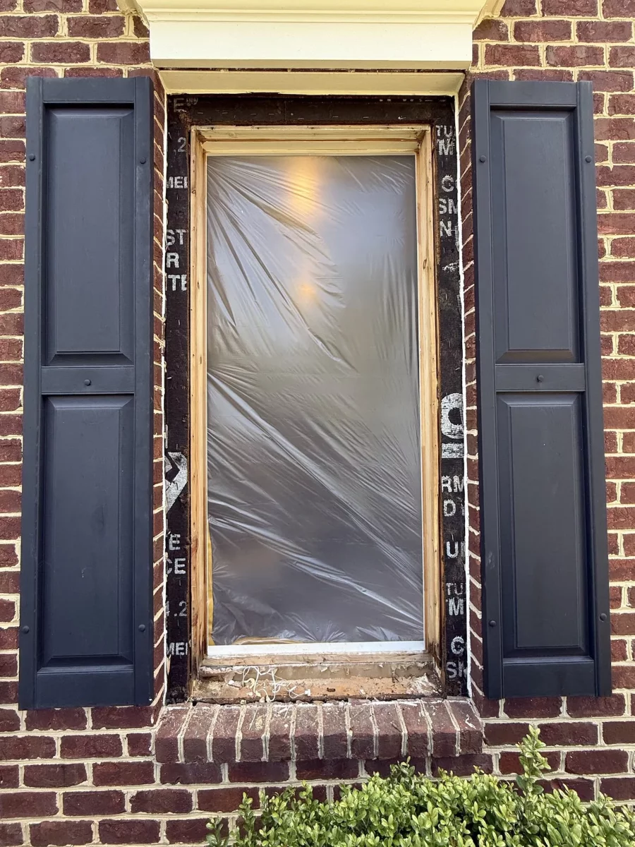 Window opening with plastic film and exposed frame on brick exterior