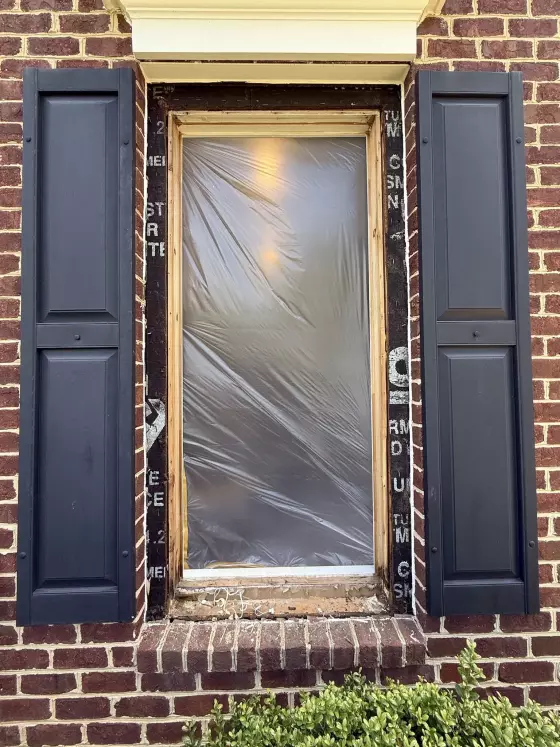 Window opening with plastic film and exposed frame on brick exterior