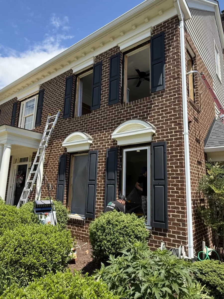 Brick house exterior with windows being replaced, ladders and workers visible