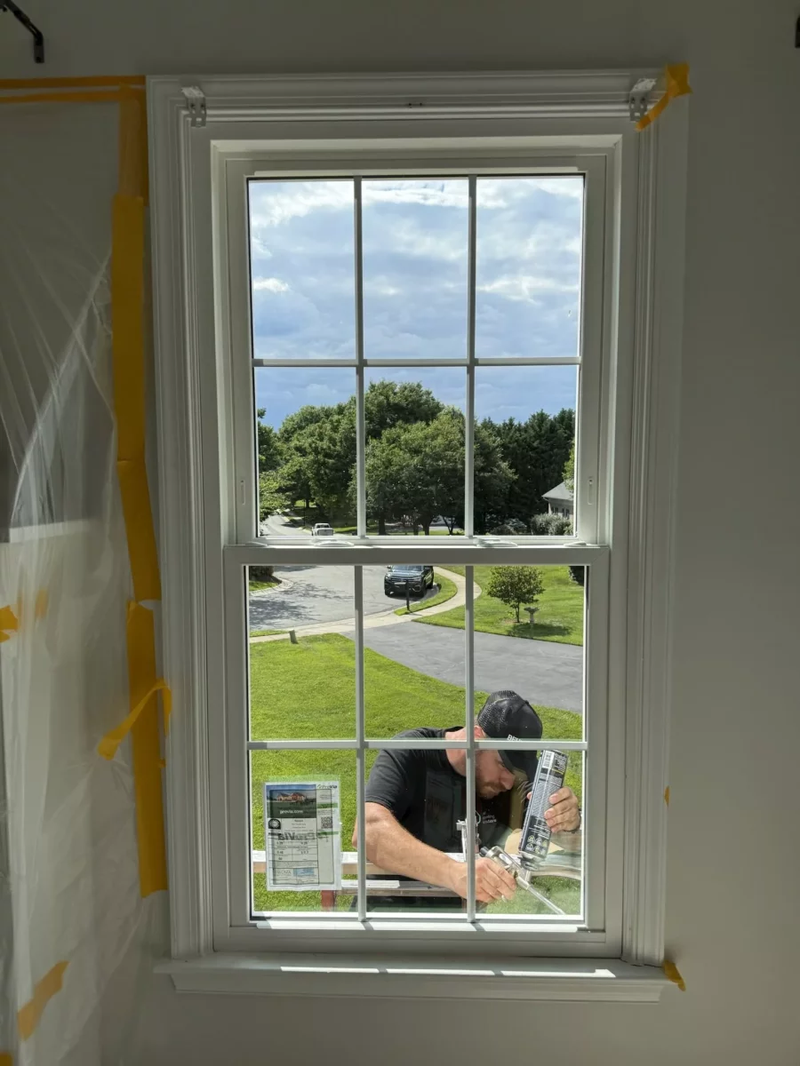 Worker installing window with caulking gun from inside residential room