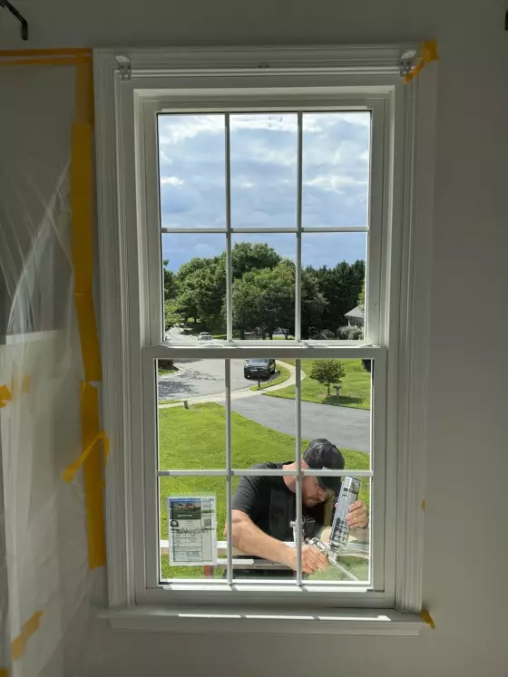Worker installing window with caulking gun from inside residential room