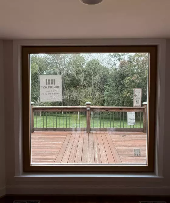 Large window with wood trim overlooking a deck and backyard