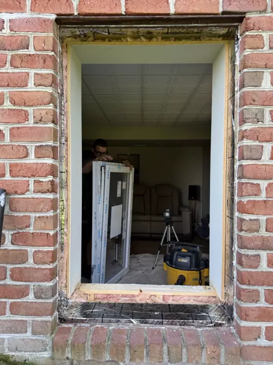 Brick exterior with window opening and worker preparing new window for installation