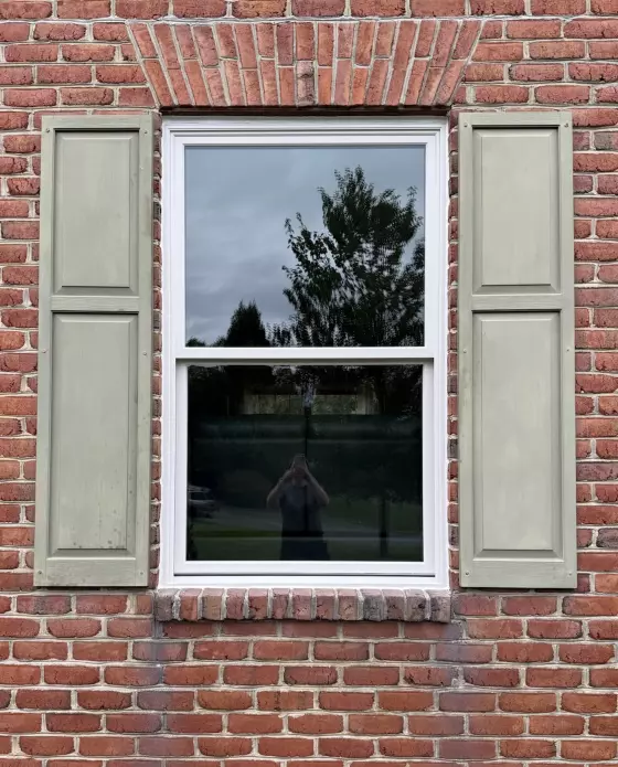 Exterior view of a double-hung window with shutters in a brick wall