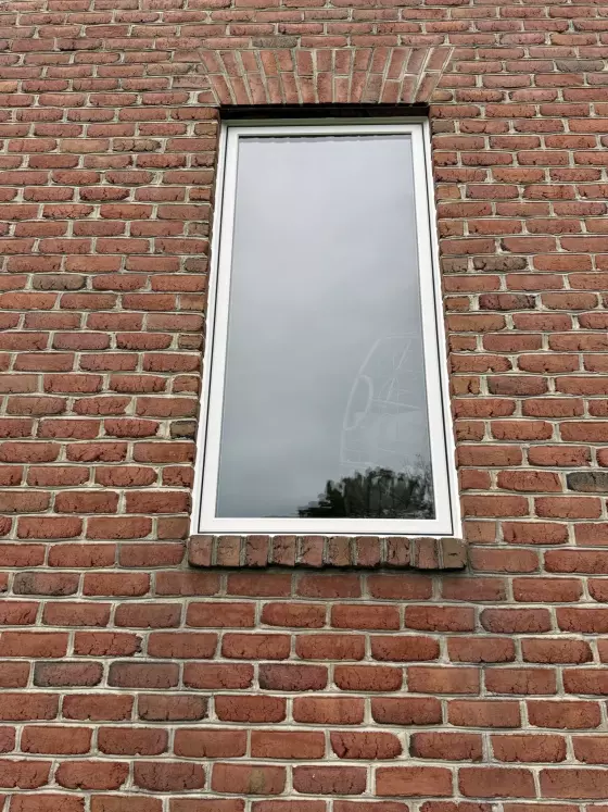 Single window with white frame in red brick exterior wall