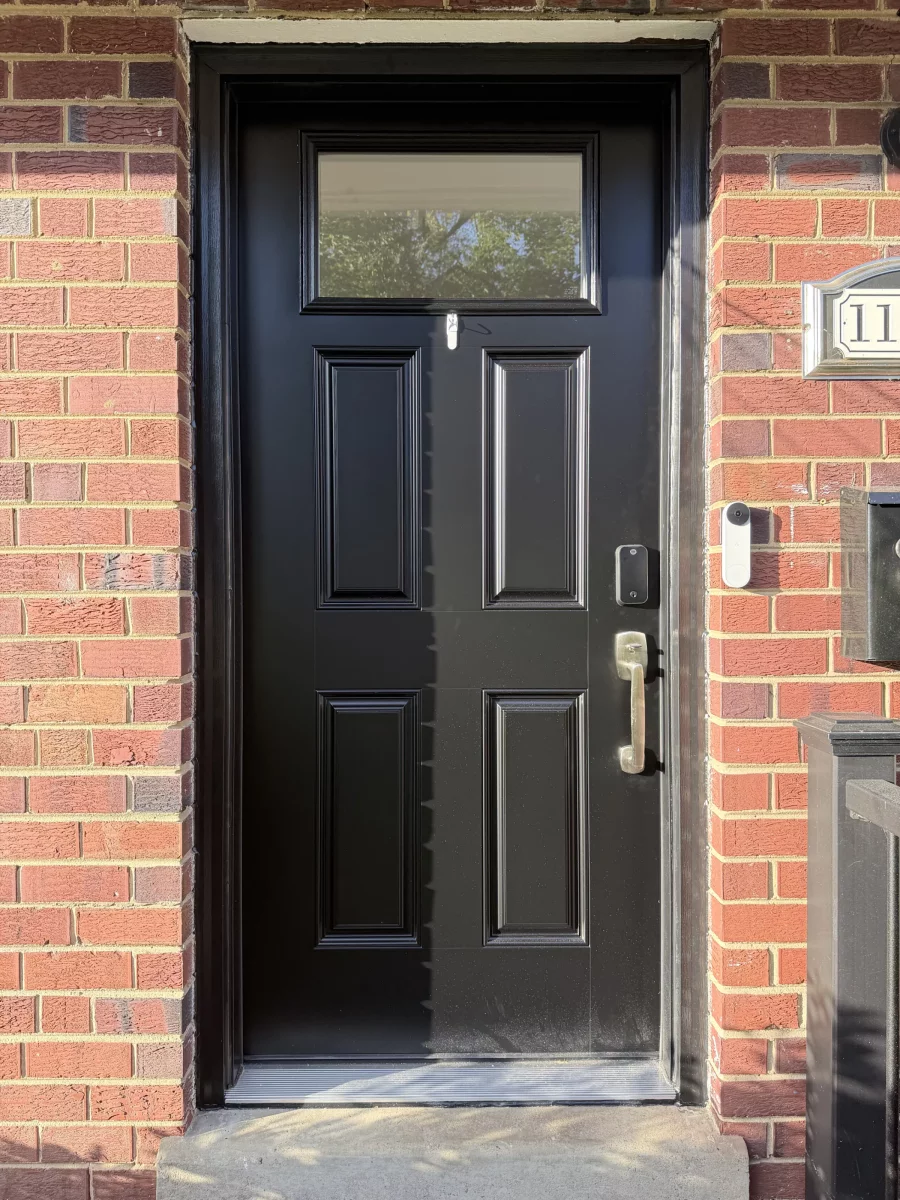 Black entry door with glass panel and handle on brick facade
