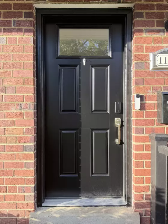 Black entry door with glass panel and handle on brick facade