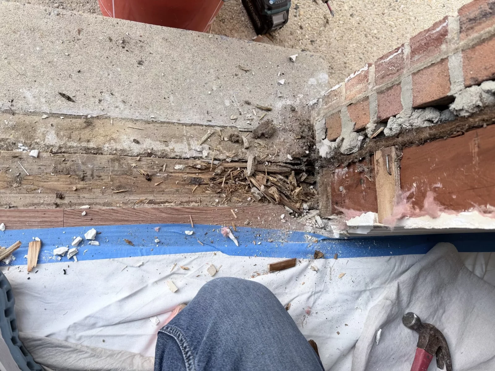 Detail of rotted wood and brick at exterior threshold with debris and tools visible