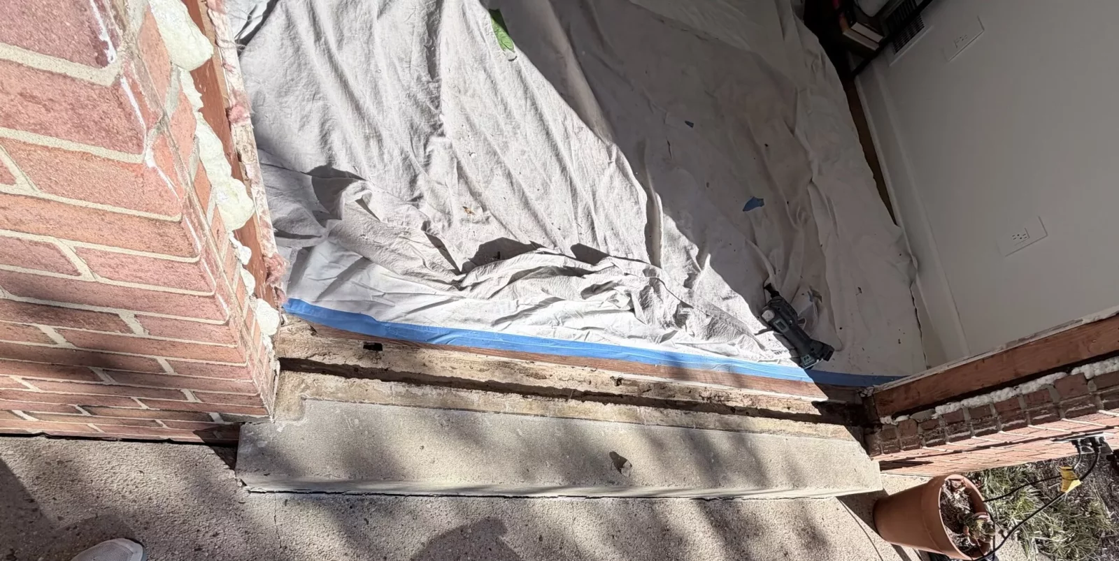 Door threshold area with brick wall, drop cloth, and power tool visible