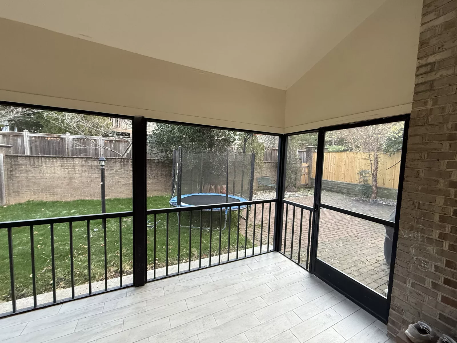 Screened patio with tiled floor and brick wall in residential backyard