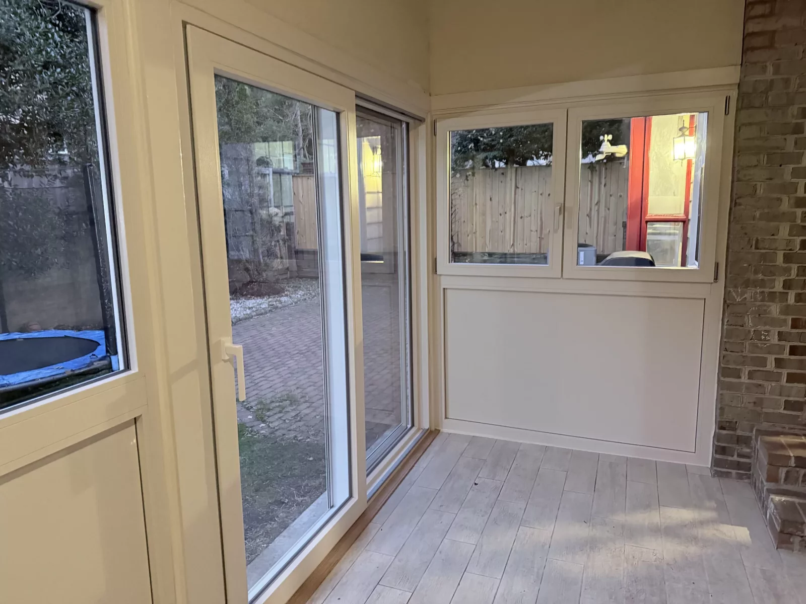 Sunroom corner with Oknoplast Compact sliding door, side window, and exposed brick wall in Potomac, MD