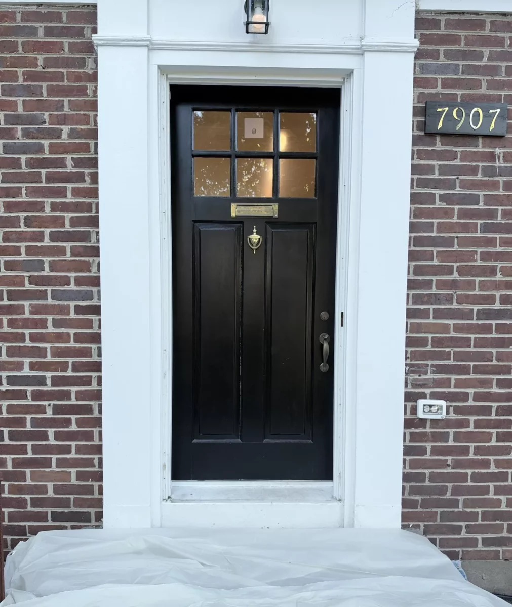 Black entry door with white trim and protective covering on ground