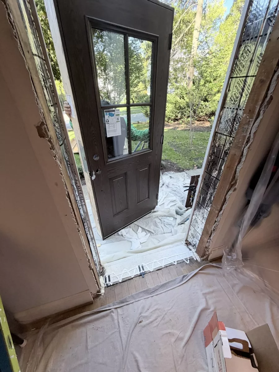 Entry door being installed with drop cloths and tools visible