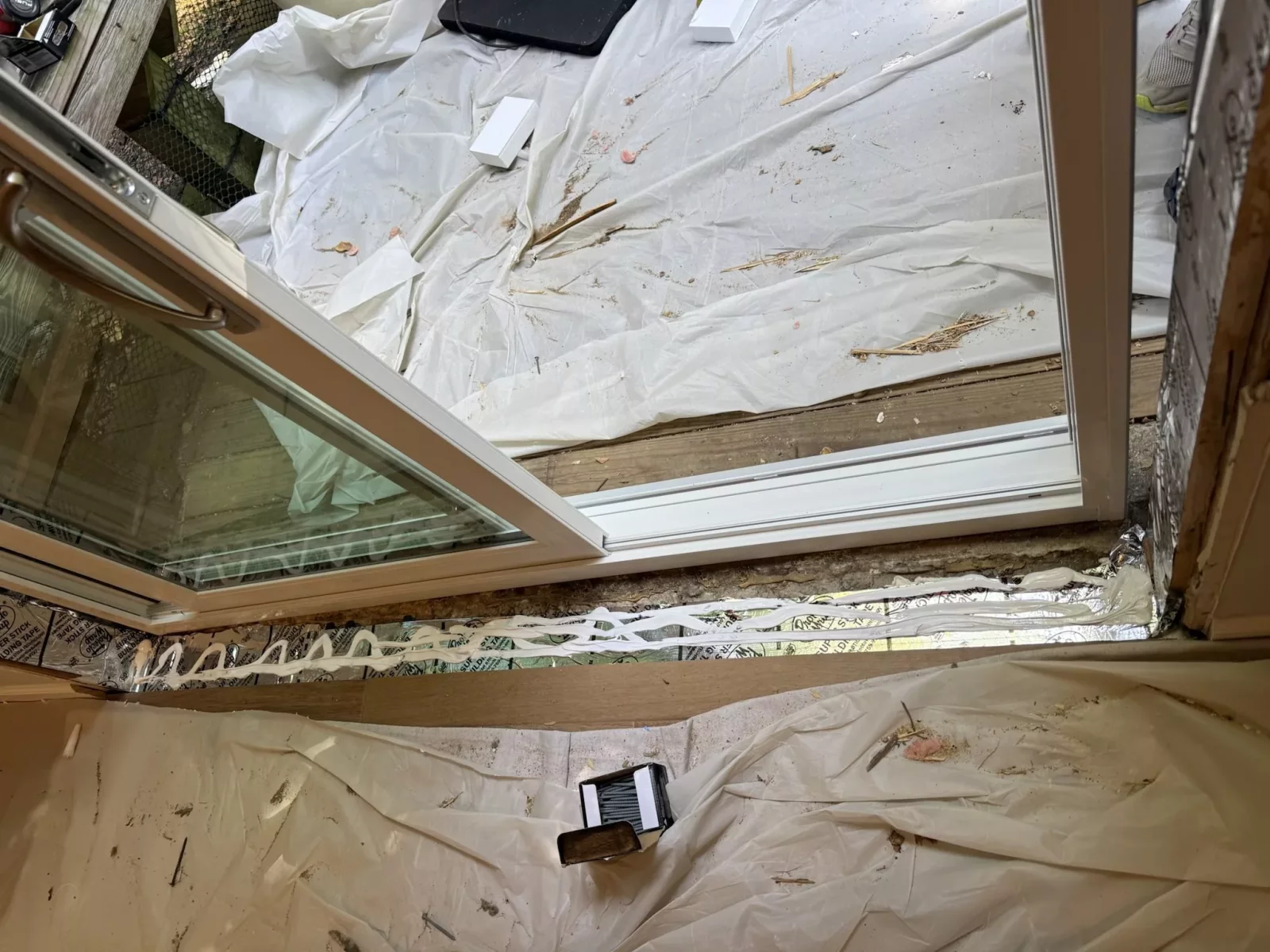 Sliding patio door installation in progress with sealant and drop cloths visible.