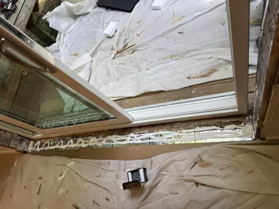 Sliding patio door installation in progress with sealant and drop cloths visible.
