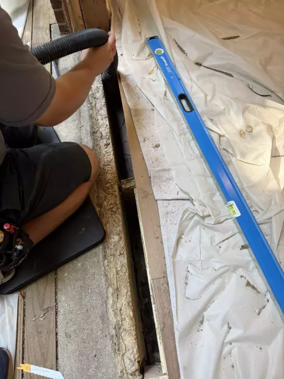 Person vacuuming debris from exposed floor section with level and drop cloth visible